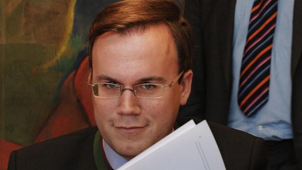 Ein Mann mit Brille hält ein paar Blätter Papier in der Hand.