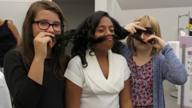 Drei Mädchen posieren mit ihren Haaren als falsche Schnurrbärte.