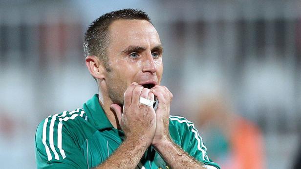 Ein Fußballspieler mit einem Verband an der Hand, der sich auf dem Spielfeld die Hand vor den Mund hält.