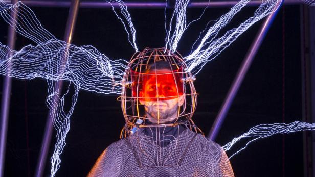 Ein Mann mit einem Metallkäfig um den Kopf, umgeben von Blitzen.