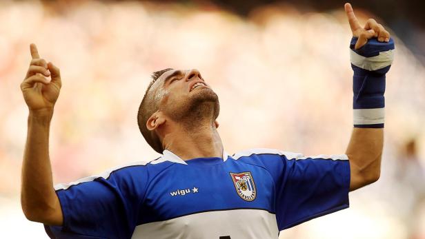 Ein Fußballspieler mit bandagiertem Arm jubelt mit erhobenen Händen.