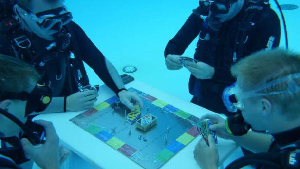 Mehrere Taucher spielen ein Brettspiel unter Wasser.