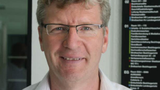 Ein Mann mit Brille und hellem Haar lächelt in die Kamera.