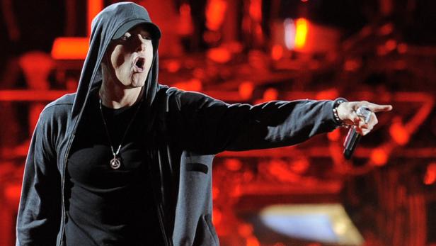 Eminem rappt mit Kapuzenpullover und Mikrofon in der Hand auf einer Bühne.