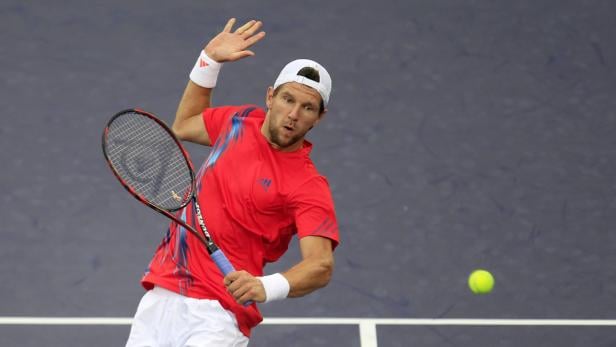 Ein Tennisspieler in rotem Hemd schlägt einen Ball.