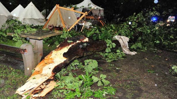 Ein abgebrochener Baumstamm liegt vor beschädigten Zelten, möglicherweise nach einem Sturm.