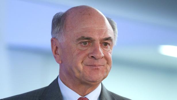 Ein Porträt eines Mannes in einem grauen Anzug und einem roten Hemd.