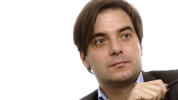 Ein Mann mit braunen Haaren und Anzug hält einen Stift in der Hand.