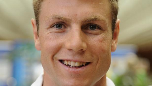 Ein lächelnder Mann mit blonden Haaren und blauen Augen blickt in die Kamera.
