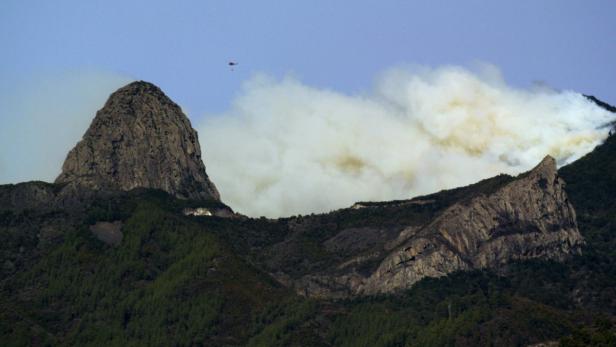 Ein Hubschrauber bekämpft einen Waldbrand in einer bergigen Landschaft.