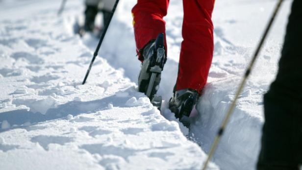 Eine Person in Skischuhen und roter Hose geht durch den Schnee.