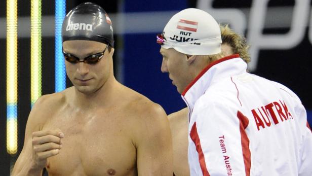 Zwei Schwimmer, einer mit Badekappe mit österreichischer Flagge, stehen nebeneinander.