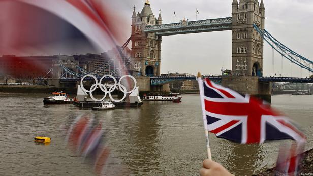 Der Tower Bridge in London mit den olympischen Ringen auf dem Fluss Themse und einer britischen Flagge im Vordergrund.