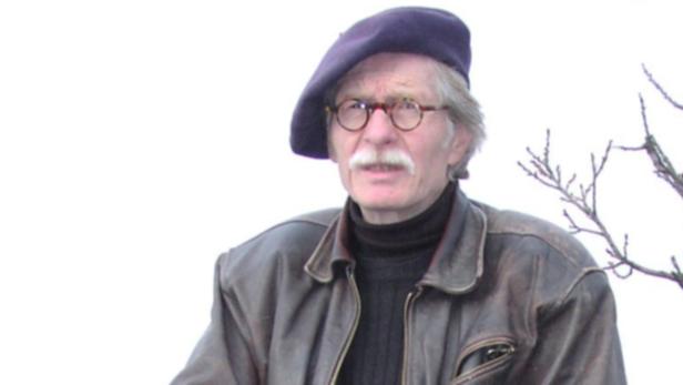 Ein älterer Mann mit Brille und Barett trägt eine Lederjacke.