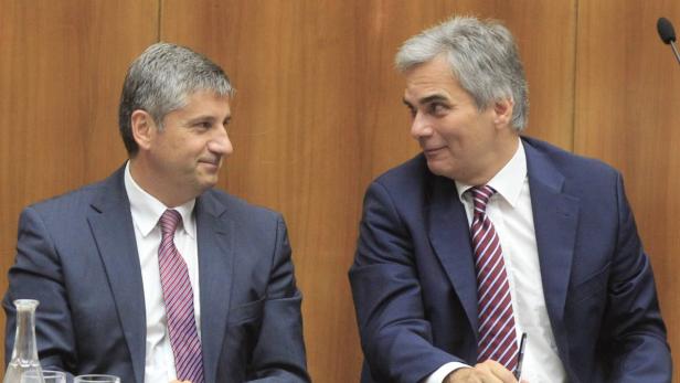 Zwei Männer in Anzügen sitzen an einem Tisch und schauen sich an.