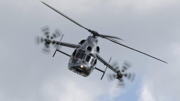 Ein grauer Hubschrauber mit gegenläufigen Rotoren ist in der Luft.
