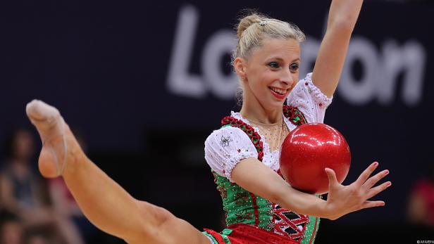 Eine rhythmische Sportgymnastin mit einem roten Ball bei einem Wettkampf.