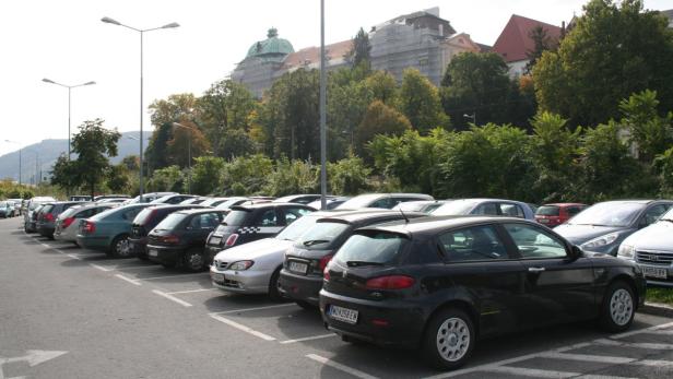 Ein Parkplatz mit vielen Autos vor einer bewaldeten Hügellandschaft.