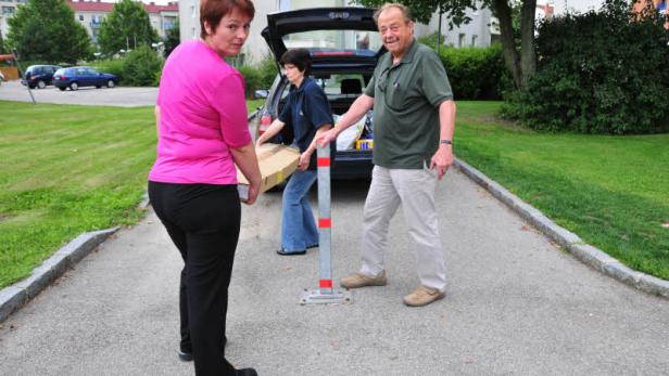 Drei Personen tragen eine Kiste zu einem Auto mit geöffnetem Kofferraum.