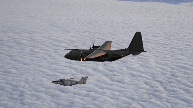 Ein Transportflugzeug und ein Jagdflugzeug fliegen über einer Wolkendecke.