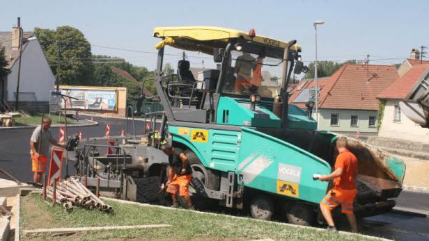 Bauarbeiter arbeiten mit einer Straßenfertigungsmaschine an einer neuen Asphaltdecke.