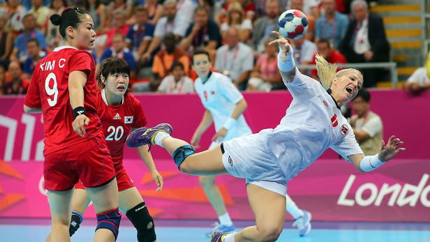 Eine Handballspielerin springt, um den Ball zu werfen, während zwei koreanische Spielerinnen zusehen.