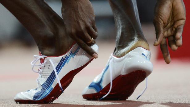 Ein Athlet bereitet sich mit Spikes-Schuhen auf einem roten Untergrund auf einen Lauf vor.