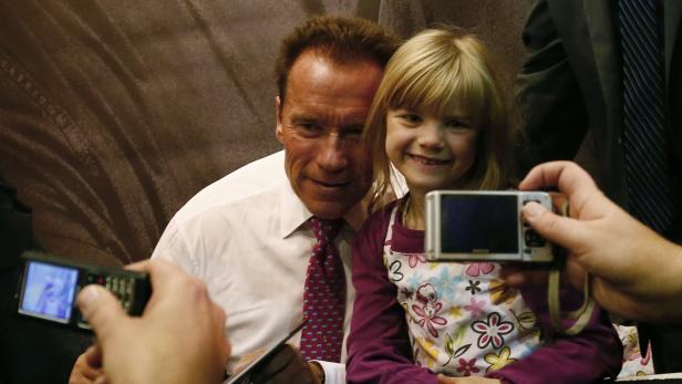 Arnold Schwarzenegger posiert mit einem jungen Mädchen für Fotos.
