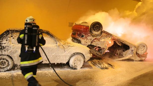 Ein Feuerwehrmann löscht zwei ineinander verkeilte und brennende Autos mit Schaum.