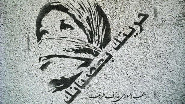 Graffito einer Frau mit Kopftuch und arabischer Schrift auf einer Wand.
