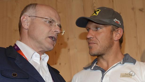 Zwei Männer stehen vor einer Holzwand und unterhalten sich.