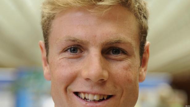 Ein lächelnder Mann mit blonden Haaren und blauen Augen blickt in die Kamera.