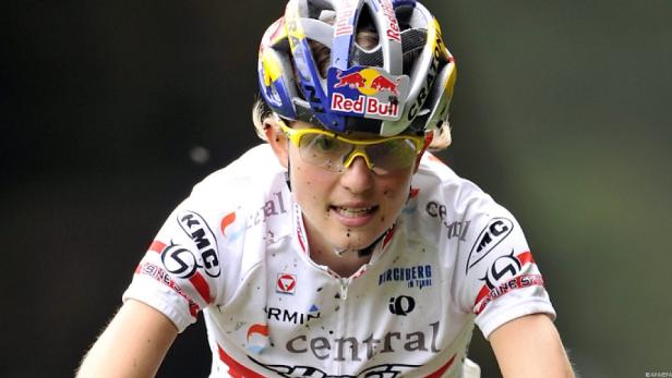Eine Mountainbikerin mit gelber Brille und Red Bull Helm ist schmutzig vom Rennen.