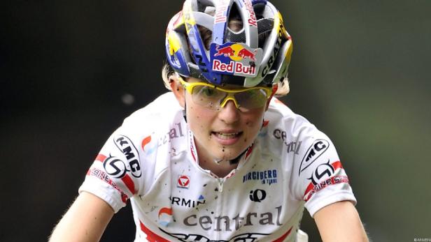 Eine Mountainbikerin mit gelber Brille und Red Bull Helm ist schmutzig vom Rennen.