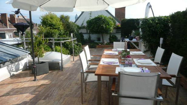 Ein gedeckter Esstisch auf einer begrünten Dachterrasse mit Sonnenschirm.
