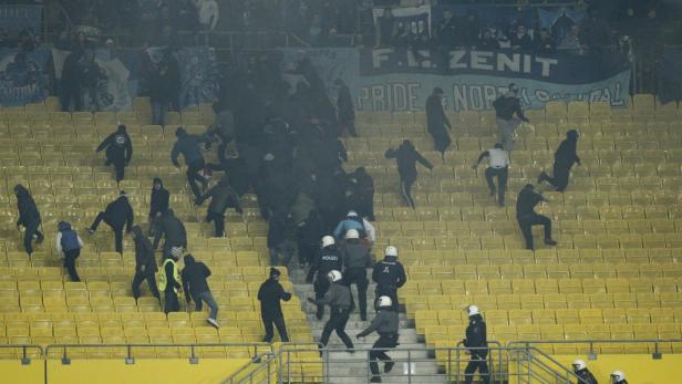Polizisten und Fans auf den gelben Tribünen eines Fußballstadions.