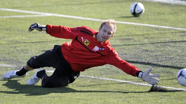 Ein Torwart hechtet auf einem grünen Rasen nach einem Fußball.