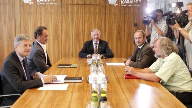 Mehrere Personen sitzen an einem Tisch während einer Pressekonferenz der Kärntner Landesregierung.