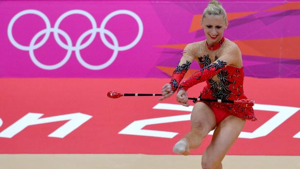 Eine rhythmische Sportgymnastin bei einer Vorführung mit Keulen vor dem Hintergrund der Olympischen Ringe.