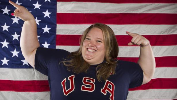 Eine Frau mit einem T-Shirt mit der Aufschrift „USA“ posiert vor der amerikanischen Flagge.