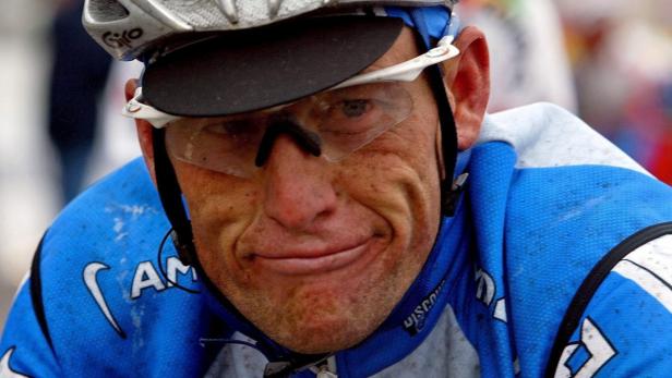 Ein erschöpfter Radrennfahrer mit Helm und Brille blickt in die Kamera.