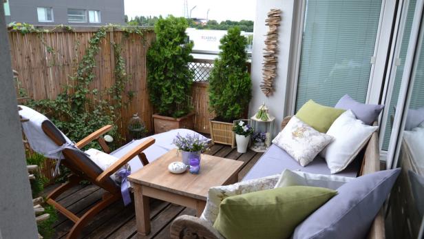 Ein gemütlicher Balkon mit Holzmöbeln, Pflanzen und Kissen lädt zum Entspannen ein.