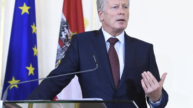 Ein Mann in Anzug spricht vor der Europa- und Österreich-Flagge.