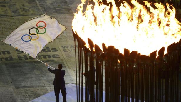 Eine Person hält die olympische Flagge neben der olympischen Flamme.