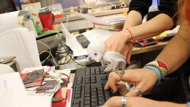 Zwei Personen tippen auf einer Computertastatur an einem unordentlichen Schreibtisch.