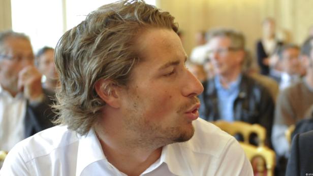 Ein Mann mit blonden Haaren spricht vor einer Gruppe von Menschen.