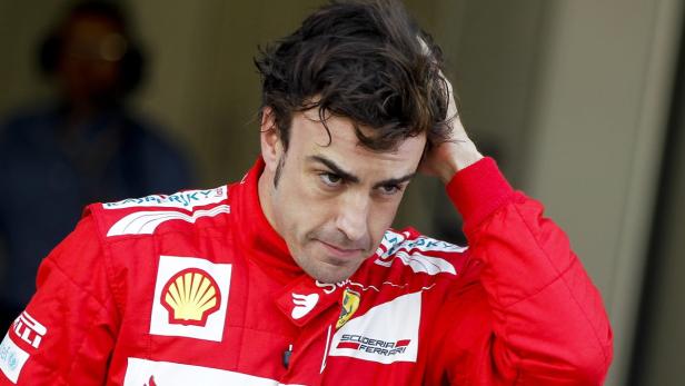 Fernando Alonso im roten Ferrari-Rennanzug blickt nachdenklich und fährt sich durch die Haare.