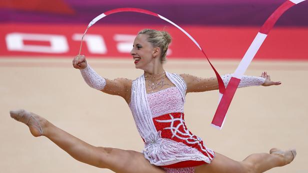 Eine rhythmische Sportgymnastin führt eine Übung mit einem rot-weißen Band vor.