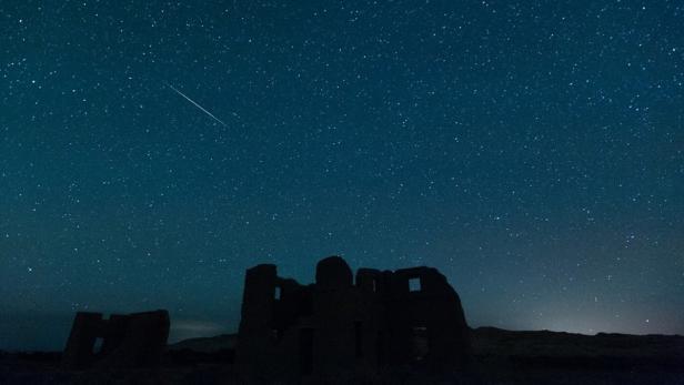 Sternenhimmel über den Ruinen eines alten Gebäudes mit einer Sternschnuppe.
