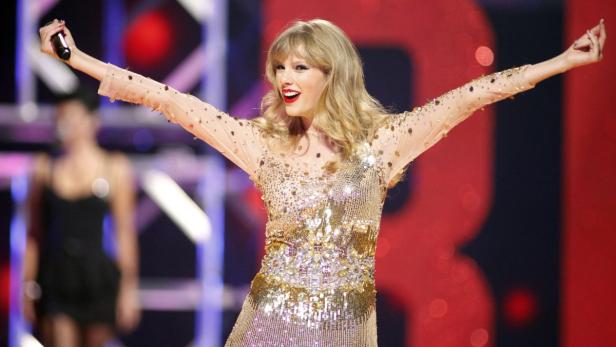Taylor Swift tritt in einem goldenen, paillettenbesetzten Kleid auf einer Bühne auf.